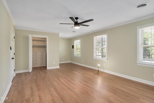 unfurnished bedroom with light wood-type flooring, a textured ceiling, ornamental molding, visible vents, and a walk in closet