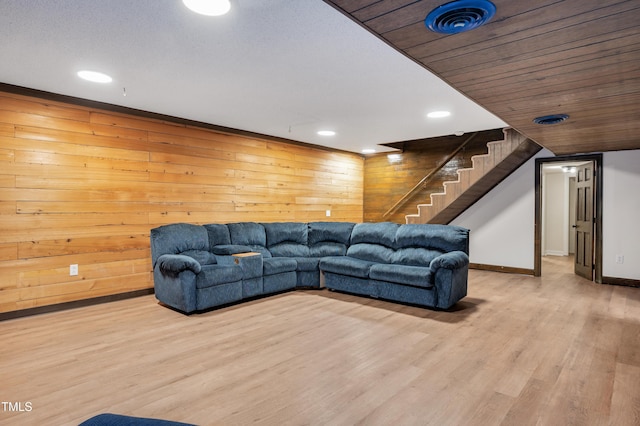 living room with light wood-style flooring, visible vents, stairway, wood walls, and baseboards
