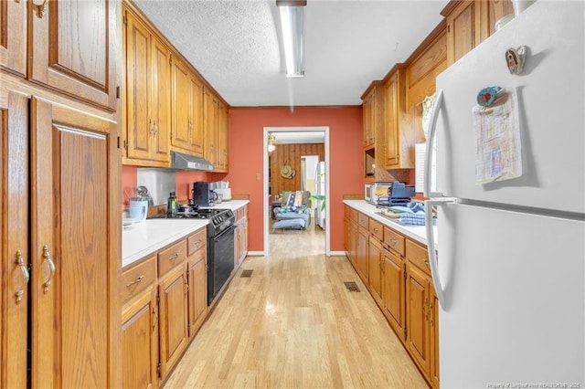 kitchen with under cabinet range hood, light countertops, freestanding refrigerator, light wood-style floors, and gas stove