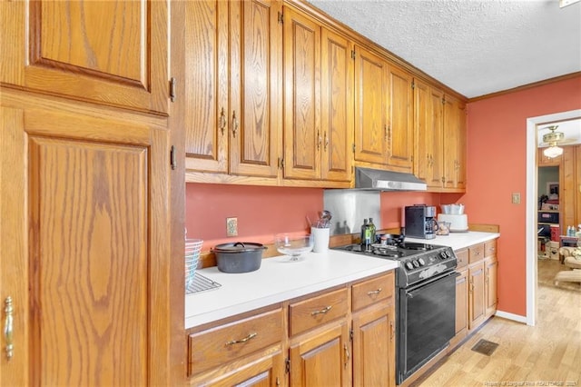 kitchen featuring black gas stove, light wood-type flooring, brown cabinets, light countertops, and under cabinet range hood