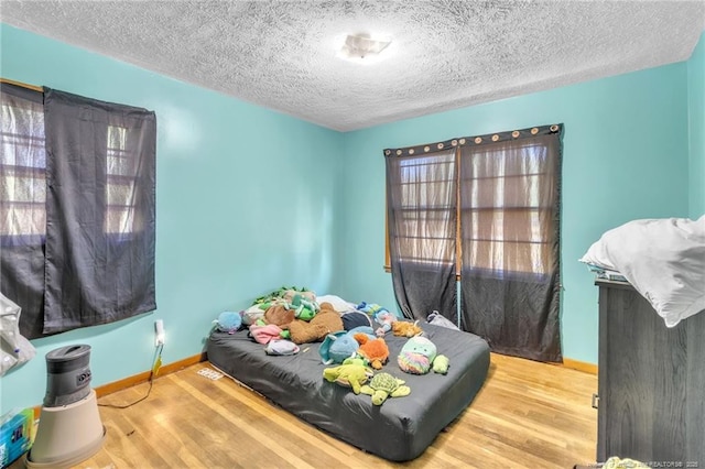 bedroom with baseboards, wood finished floors, and a textured ceiling