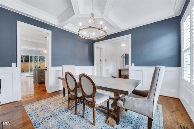 dining room with coffered ceiling, a decorative wall, an inviting chandelier, and wainscoting