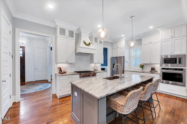kitchen featuring crown molding, a kitchen bar, a sink, stainless steel appliances, and premium range hood