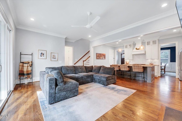 living area with ornamental molding, a ceiling fan, recessed lighting, stairway, and light wood finished floors