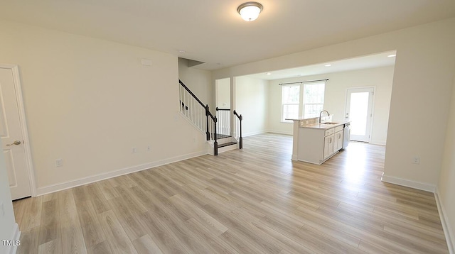 unfurnished living room with stairway, a sink, light wood finished floors, baseboards, and recessed lighting