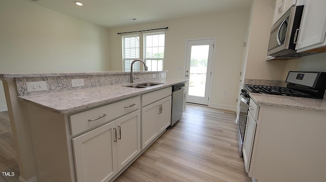 kitchen with white cabinets, a kitchen island with sink, a sink, light wood-type flooring, and appliances with stainless steel finishes