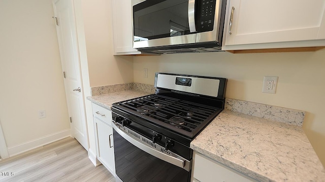 kitchen with light wood finished floors, light stone countertops, white cabinetry, and appliances with stainless steel finishes