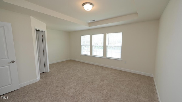 unfurnished bedroom with light carpet, a tray ceiling, visible vents, and baseboards