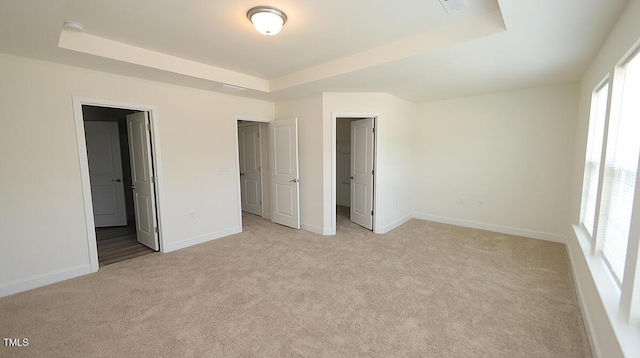 unfurnished bedroom with light carpet, a raised ceiling, and multiple windows