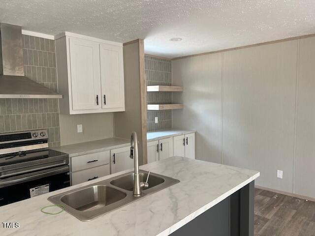 kitchen with a sink, a textured ceiling, stainless steel range with electric cooktop, decorative backsplash, and wall chimney range hood