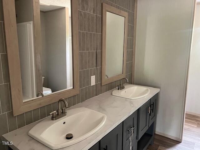 bathroom with double vanity, toilet, wood finished floors, and a sink