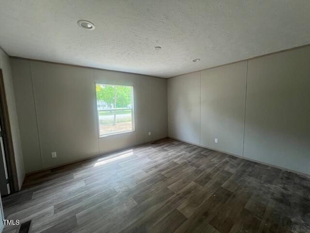 spare room with a decorative wall, wood finished floors, a textured ceiling, and visible vents