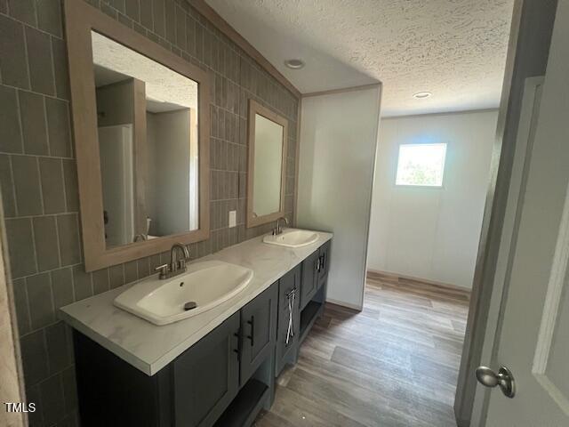full bathroom featuring wood finished floors, a sink, a textured ceiling, and double vanity