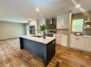 4285 Autry Mill Rd, Godwin, NC 28344 - kitchen featuring wall chimney exhaust hood, stainless steel appliances, light countertops, a kitchen island with sink, and light wood-type flooring