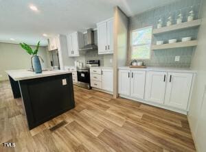 4285 Autry Mill Rd, Godwin, NC 28344 - kitchen with wall chimney range hood, electric range, white cabinets, light countertops, and wood finished floors