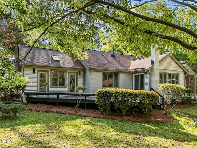 back of property featuring brick siding, a wooden deck, a lawn, and roof with shingles