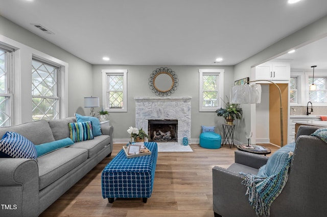 living room featuring baseboards, recessed lighting, visible vents, a high end fireplace, and wood finished floors