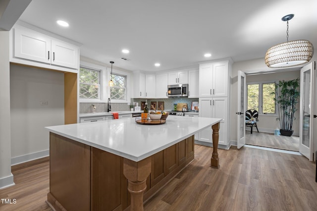 kitchen with stainless steel microwave, baseboards, backsplash, white cabinets, and dark wood finished floors