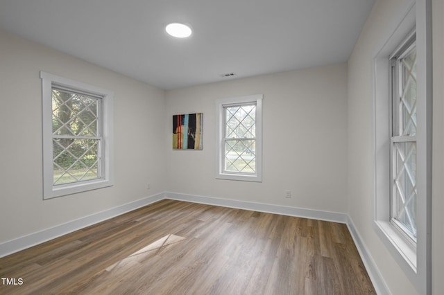 empty room featuring a wealth of natural light, visible vents, baseboards, and wood finished floors