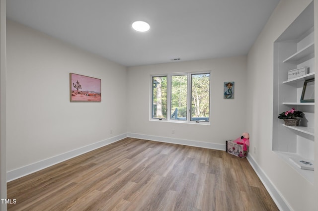 spare room with visible vents, built in features, baseboards, and wood finished floors