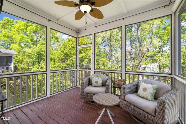 sunroom / solarium featuring ceiling fan, healthy amount of natural light, and view of wooded area