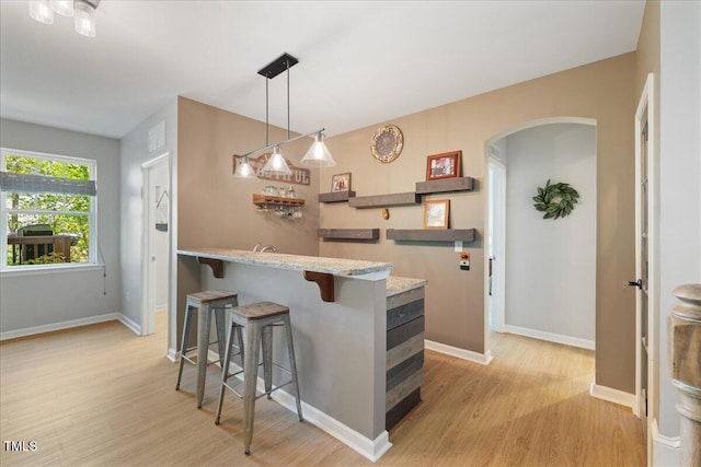 kitchen featuring arched walkways, light wood-style floors, a kitchen breakfast bar, and baseboards