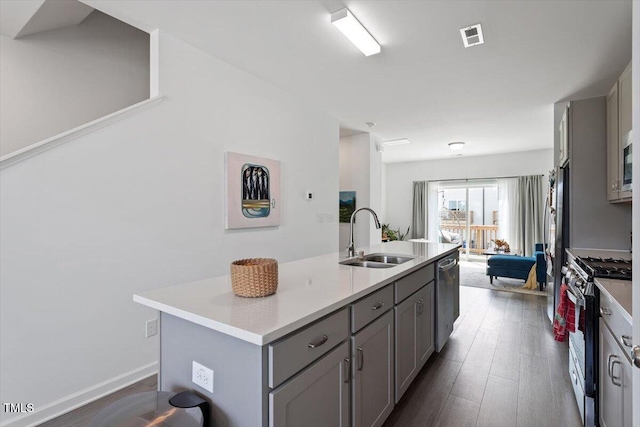 kitchen featuring stainless steel appliances, a sink, a center island with sink, gray cabinetry, and light countertops