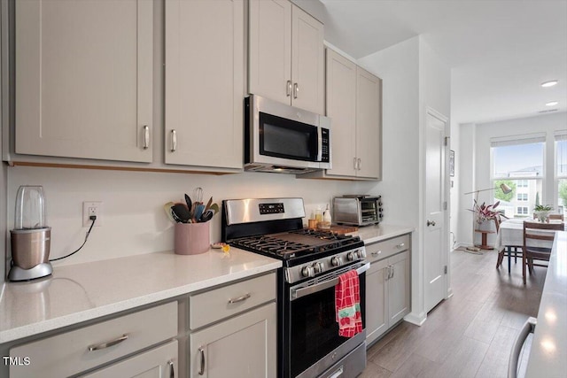 kitchen featuring wood finished floors, stainless steel appliances, light countertops, gray cabinetry, and recessed lighting
