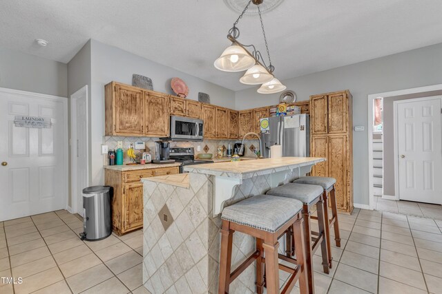 9332 Leslieshire Dr, Raleigh, NC 27615 - kitchen with an island with sink, light tile patterned floors, light countertops, decorative light fixtures, and stainless steel appliances