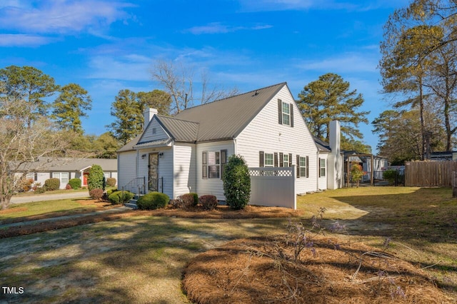 view of side of property with fence, a chimney, a yard, and metal roof