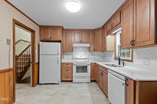 kitchen featuring white appliances, a textured ceiling, under cabinet range hood, brown cabinetry, and a sink