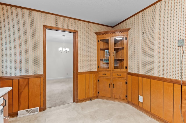 unfurnished dining area featuring crown molding, a notable chandelier, visible vents, and a wainscoted wall