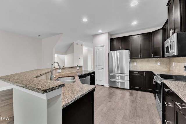 kitchen with stainless steel appliances, a sink, light wood-style flooring, a center island with sink, and recessed lighting