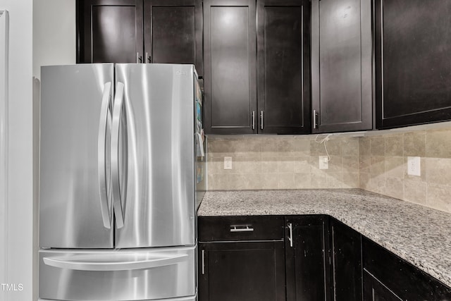 kitchen with freestanding refrigerator, backsplash, light stone countertops, and dark brown cabinets