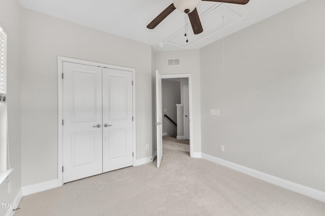 unfurnished bedroom with attic access, light carpet, a closet, baseboards, and ceiling fan