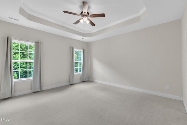 spare room with a raised ceiling, ceiling fan, light colored carpet, healthy amount of natural light, and ornamental molding