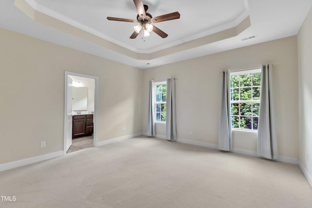 empty room with a raised ceiling, ceiling fan, ornamental molding, light colored carpet, and baseboards