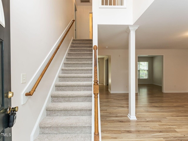 stairway featuring baseboards, wood finished floors, visible vents, and decorative columns