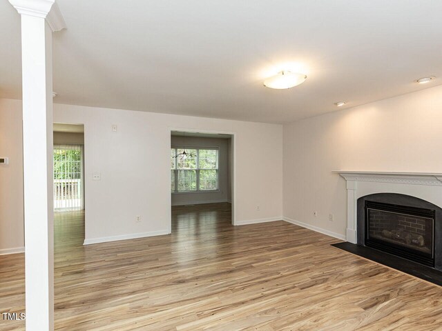 unfurnished living room with light wood finished floors, a fireplace with flush hearth, baseboards, and a healthy amount of sunlight