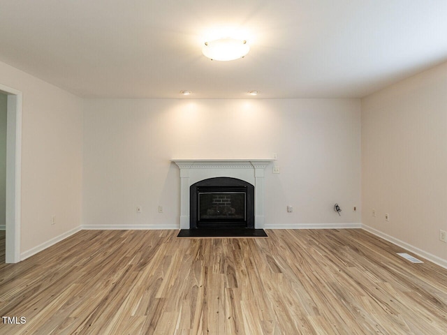 unfurnished living room featuring a fireplace with flush hearth, light wood-style floors, visible vents, and baseboards