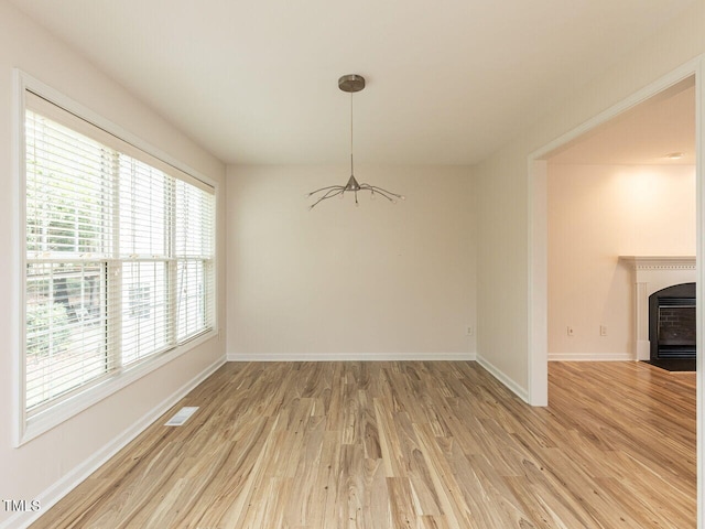 unfurnished dining area with a fireplace with flush hearth, baseboards, visible vents, and light wood finished floors