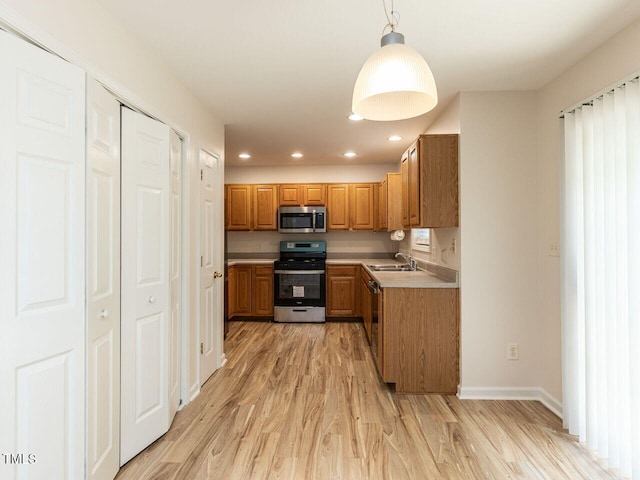 kitchen with brown cabinets, light wood finished floors, light countertops, a sink, and appliances with stainless steel finishes
