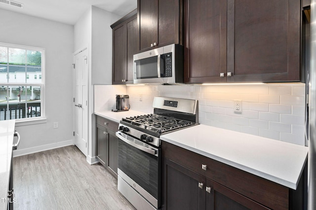 kitchen with dark brown cabinets, light wood-type flooring, light countertops, backsplash, and appliances with stainless steel finishes