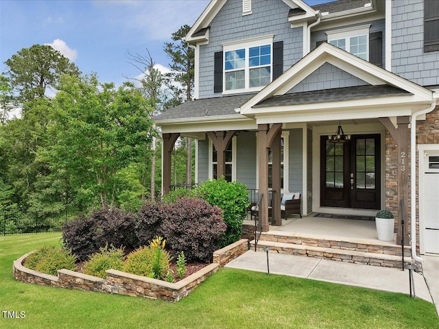 doorway to property with a porch, a lawn, and a shingled roof
