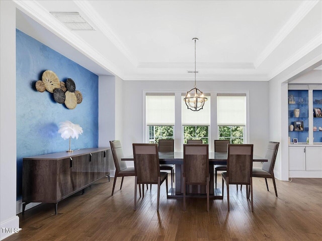 dining room featuring a raised ceiling, a chandelier, dark wood-style flooring, an accent wall, and ornamental molding