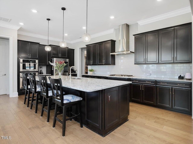 kitchen with wall chimney exhaust hood, stainless steel appliances, a kitchen bar, light stone countertops, and tasteful backsplash