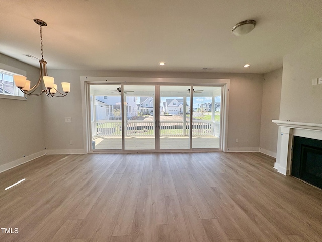 unfurnished living room featuring a healthy amount of sunlight, an inviting chandelier, baseboards, and wood finished floors