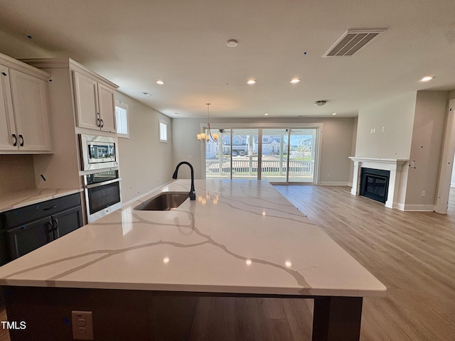 kitchen featuring visible vents, a sink, open floor plan, stainless steel appliances, and a large island with sink