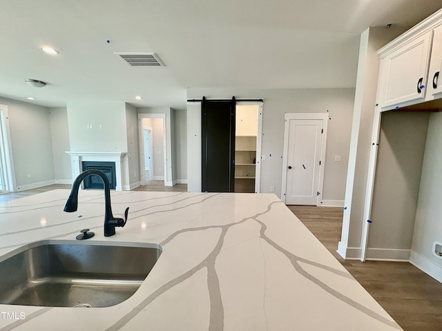 kitchen featuring white cabinets, a barn door, wood finished floors, a sink, and open floor plan