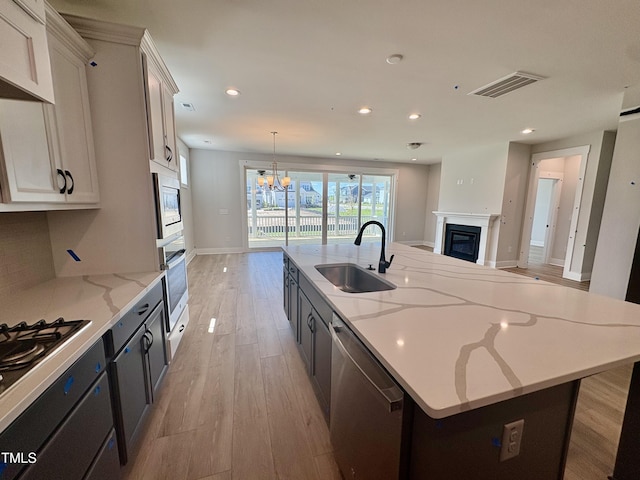 kitchen featuring a large island with sink, a glass covered fireplace, visible vents, a sink, and stainless steel appliances